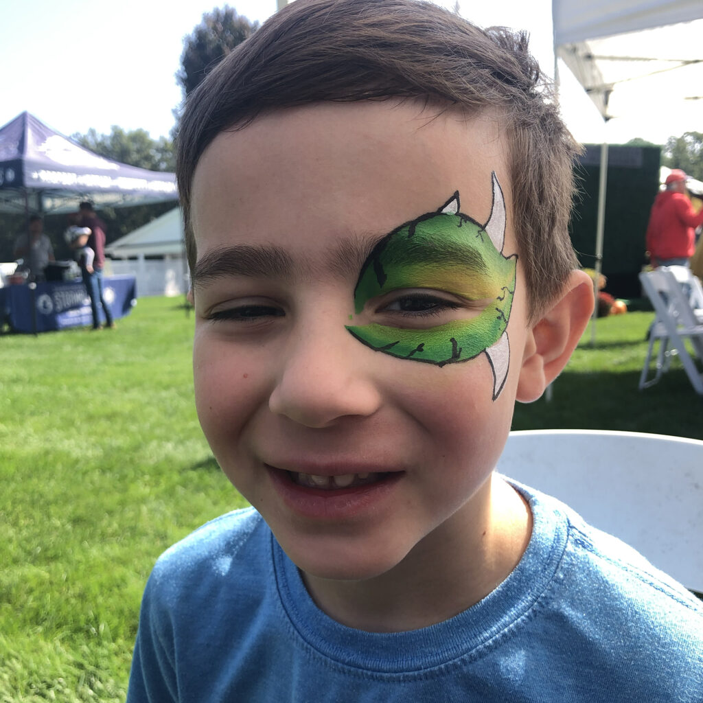 Smiling child with simple monster face painting from face painting Rhode Island at a local carnival