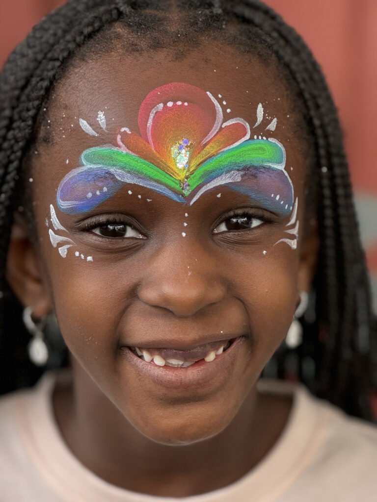 Smiling girl with rainbow face painting by face painter RI at a family gathering.