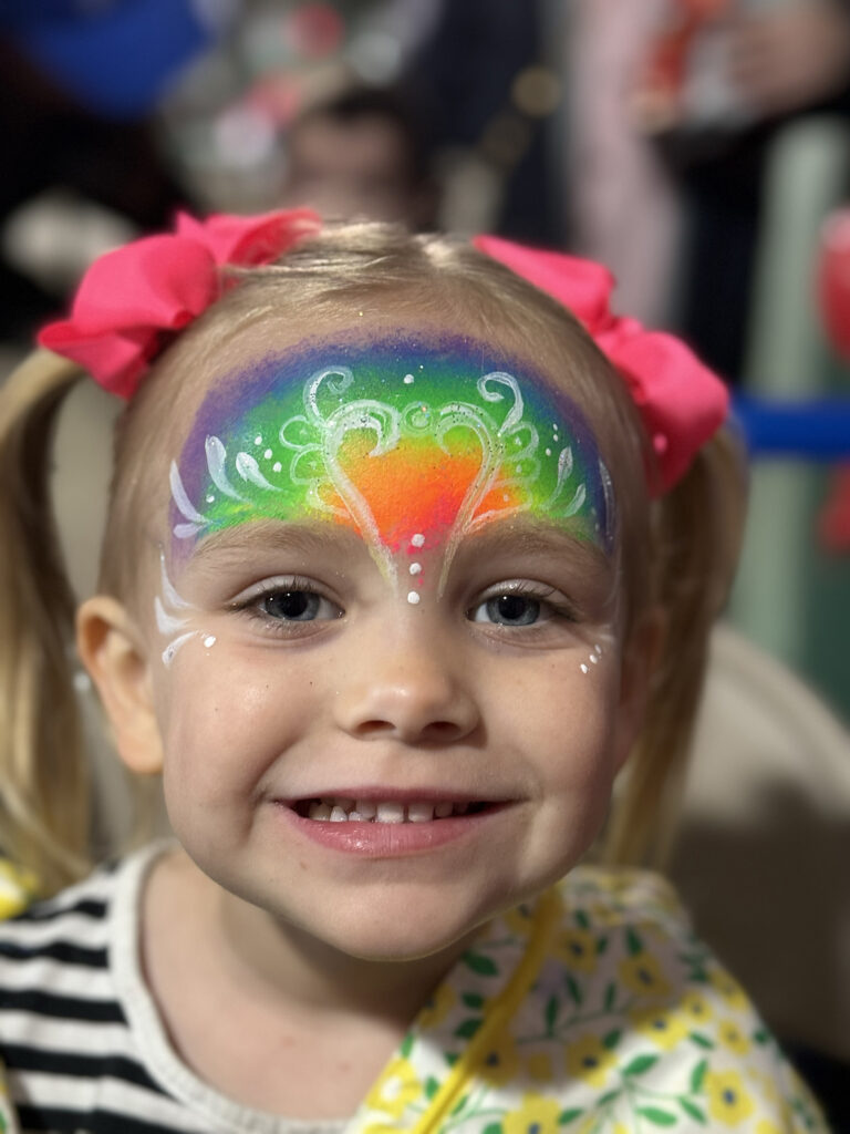 Child with rainbow face painting from face painting Rhode Island at a fun-filled celebration