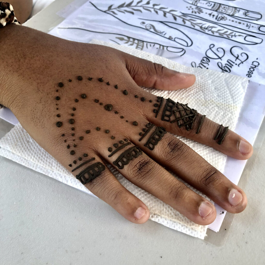 Hand featuring an ornate geometric henna design by henna artist RI, shown on a white table