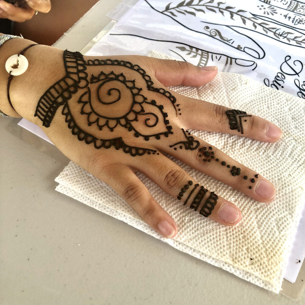 Elegant hand adorned with traditional henna by henna artist Rhode Island, set against a white table