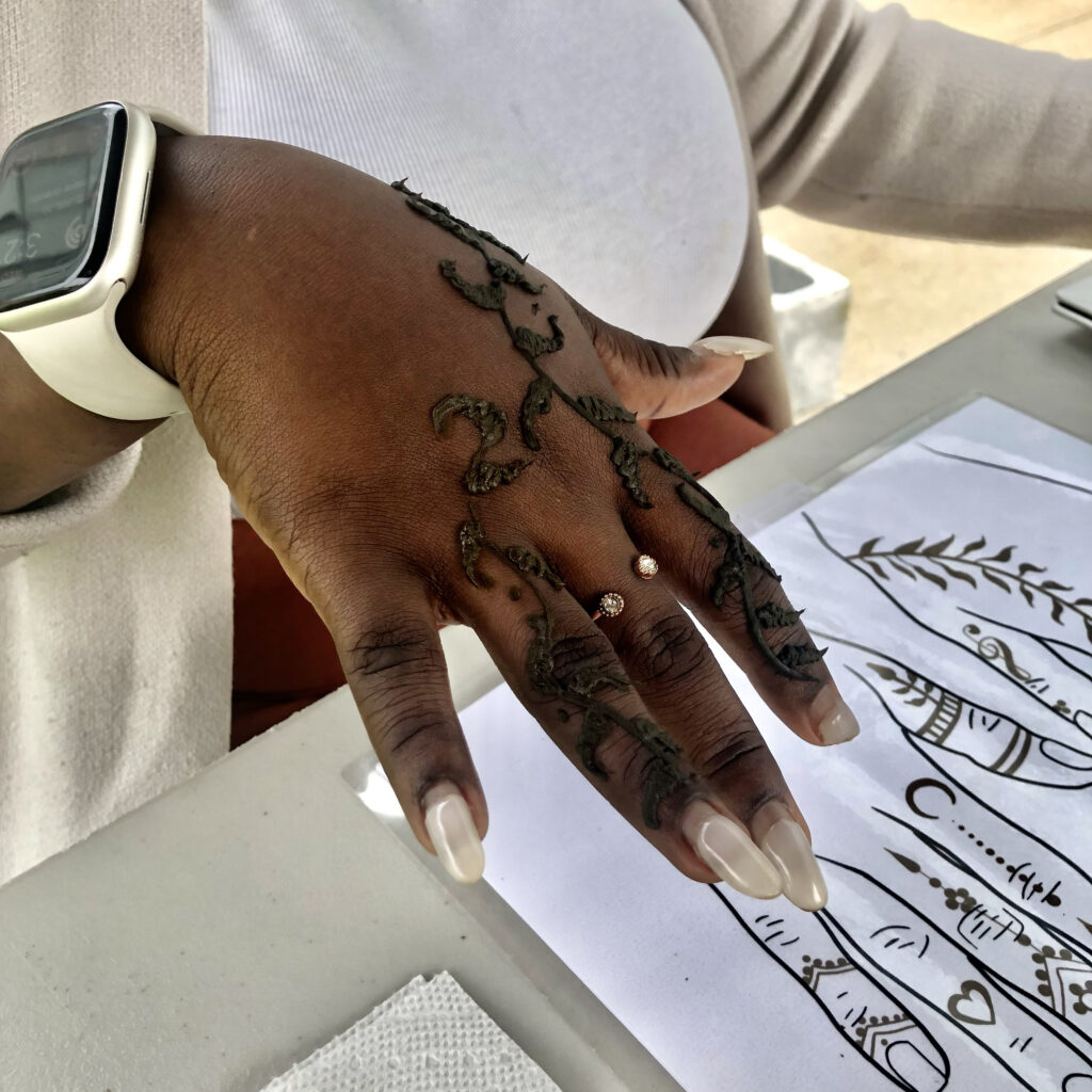 Vining henna design on a hand with dark skin, posed on a white table