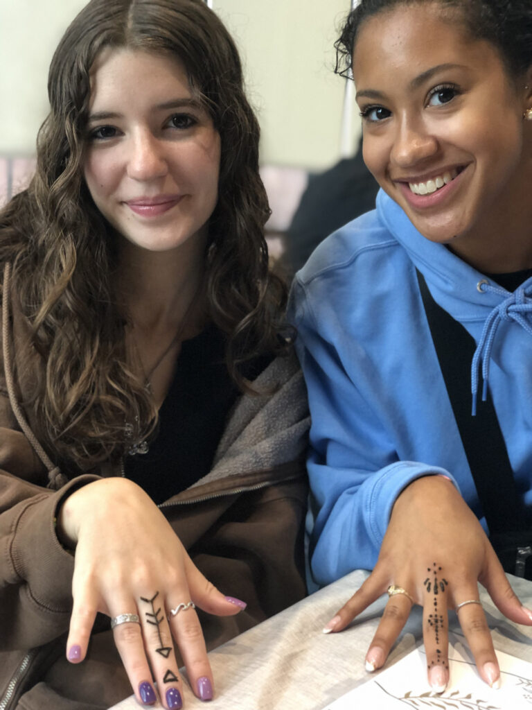 Two teen girls laughing and showing off their minimal, single finger designs at an outdoor party