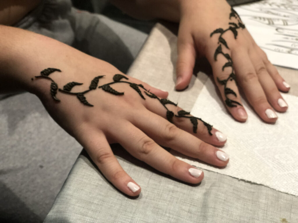 Two hands featuring a delicate floral henna design and white nail polish by henna artist Rhode Island on a white table