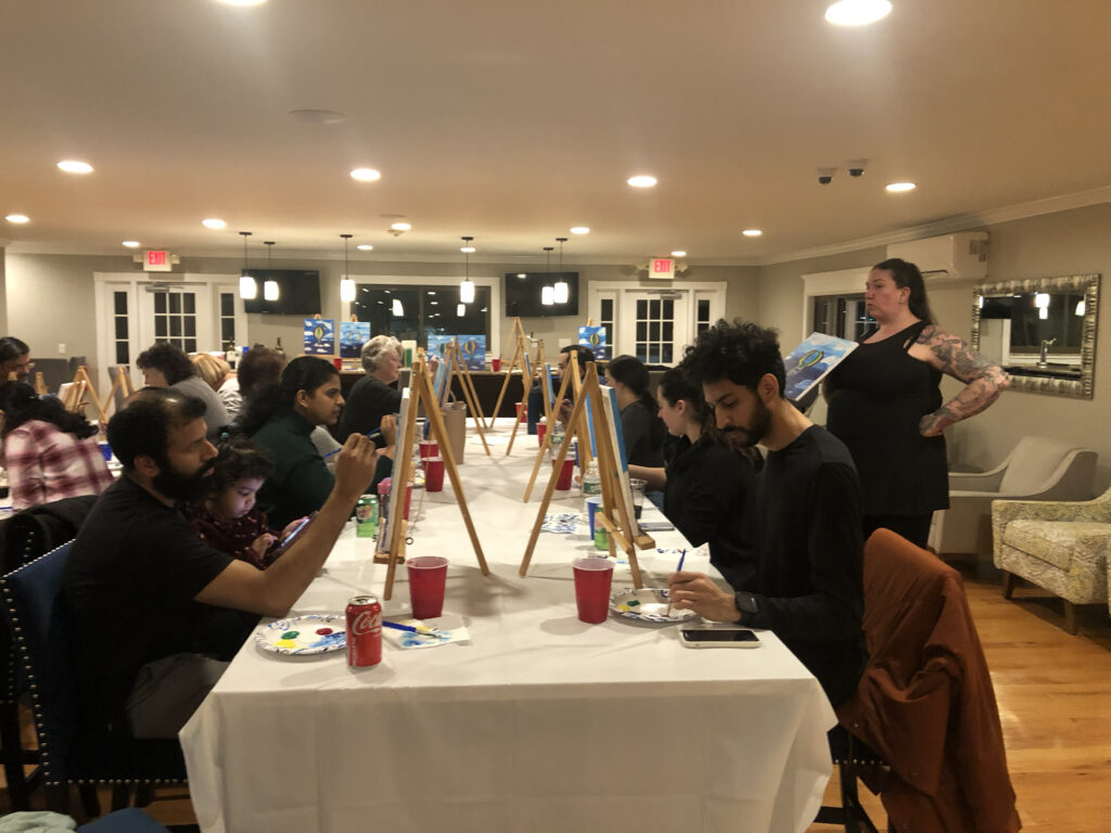 A paint night instructor showing an example to a group of adults painting canvases as a group