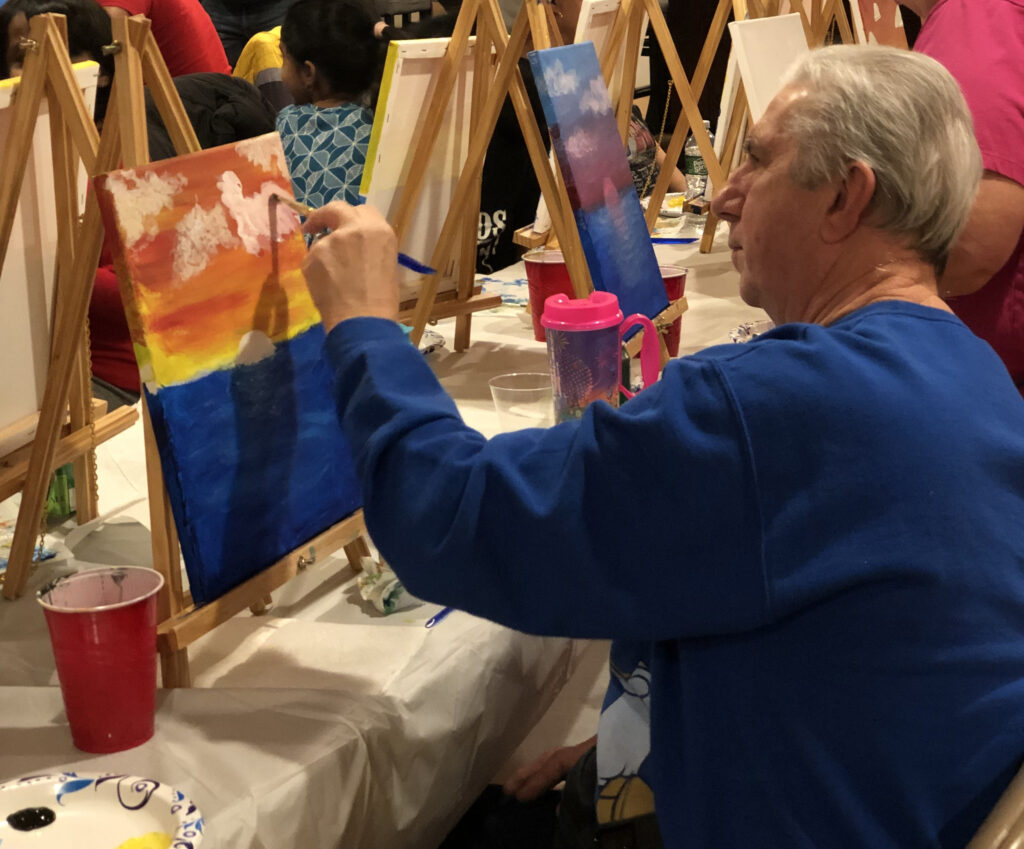 A man painting a seascape sunset at a paint night party in RI