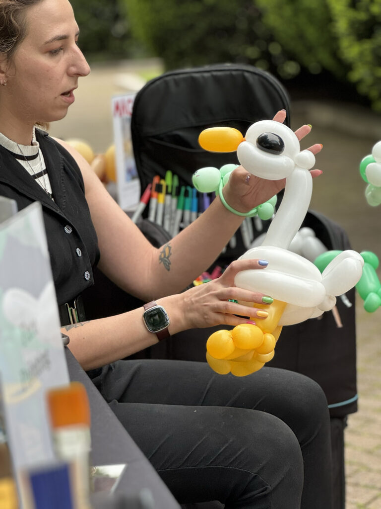 A balloon twister from Face Painter RI holding a duck balloon animal as she works at an outdoor event